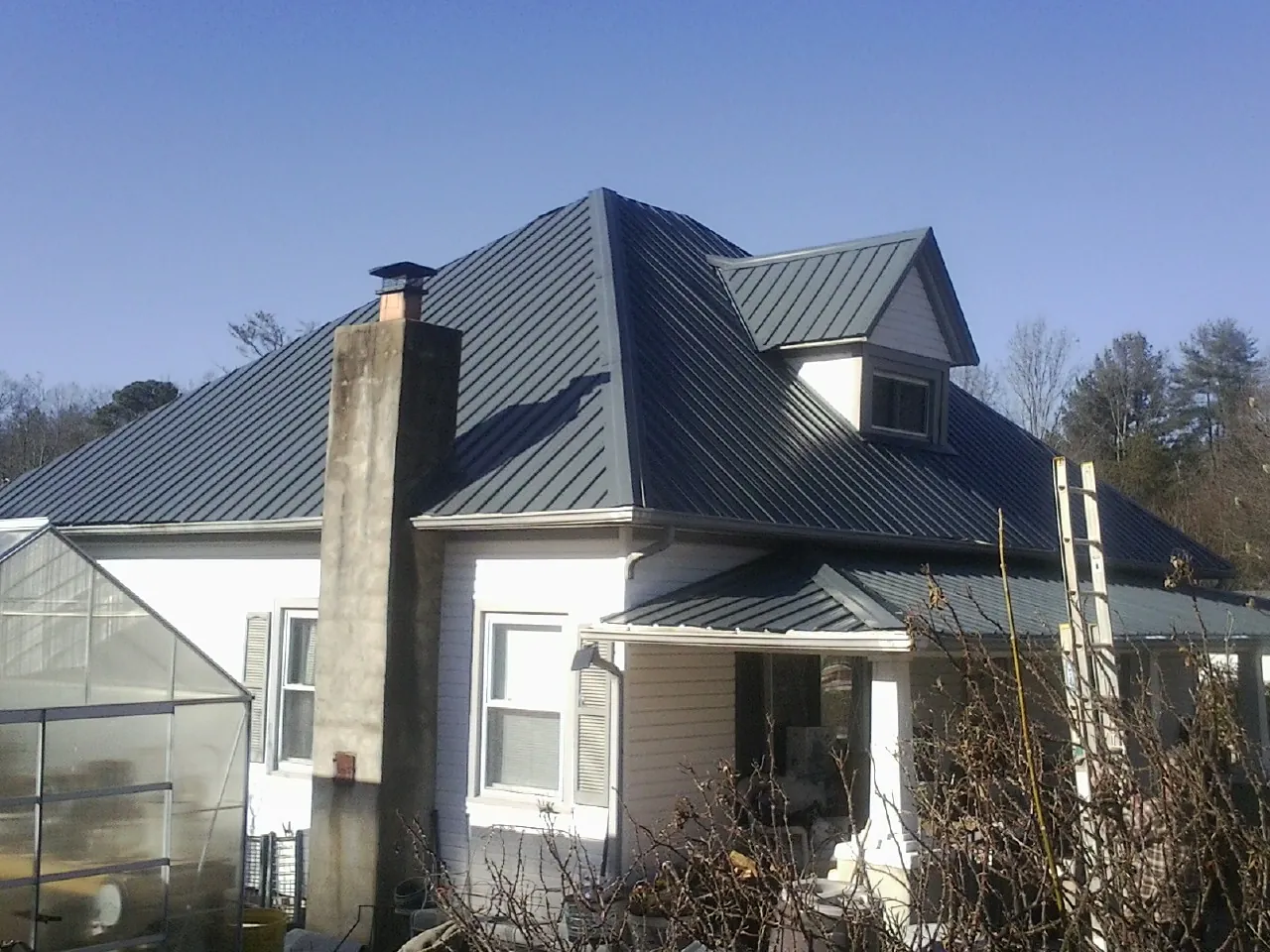 Dark blue standing seam metal roof on a white farmhouse with dormer — Slate & Tile Roof Repair by Roofing Brothers in Bahama