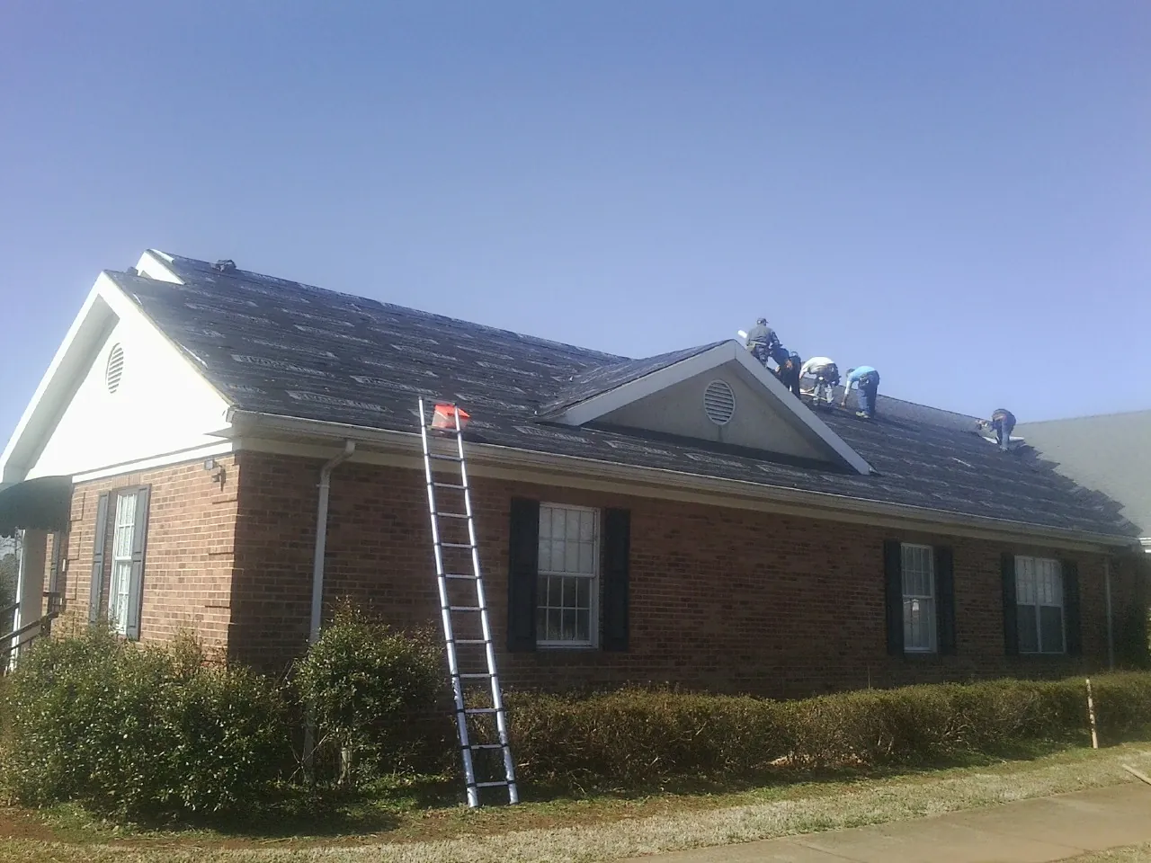 Crew tearing shingles off a brick ranch roof with a ladder set — Metal Roof Repair work by our crew in Bahama