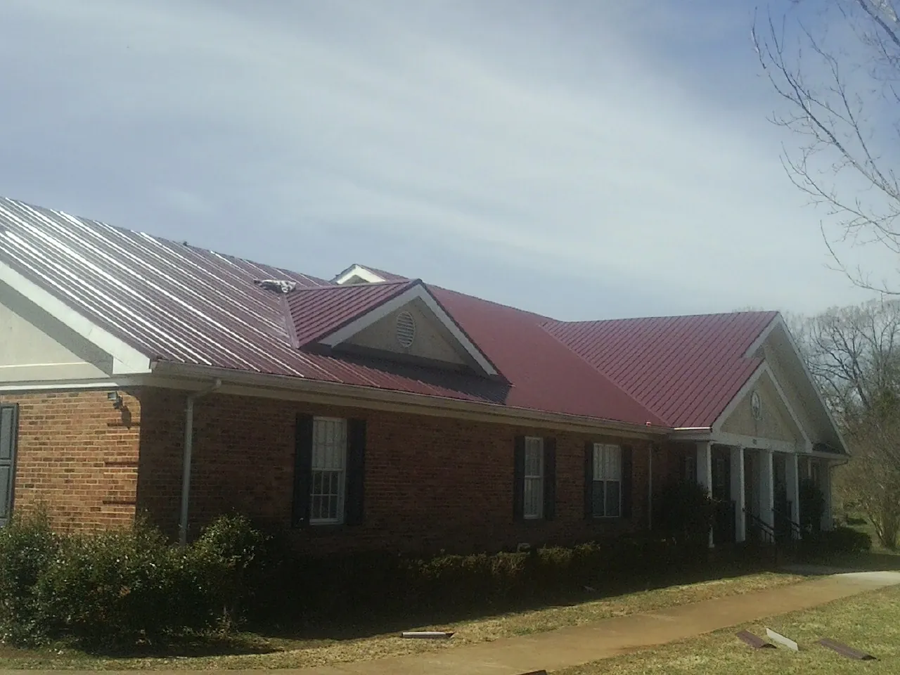 Red metal roof with gabled entries on a long brick building, from a Hail Damage Roof Repair job in Bahama