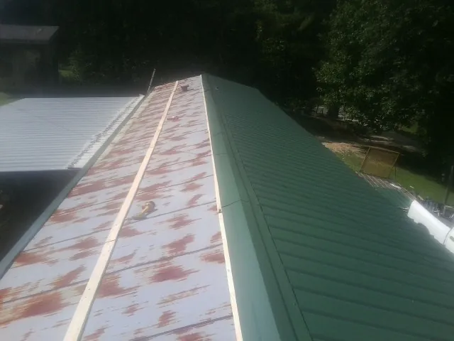 Old rusted panels beside newly installed green metal roofing — Wind Damage Roof Repair by Roofing Brothers in Bahama