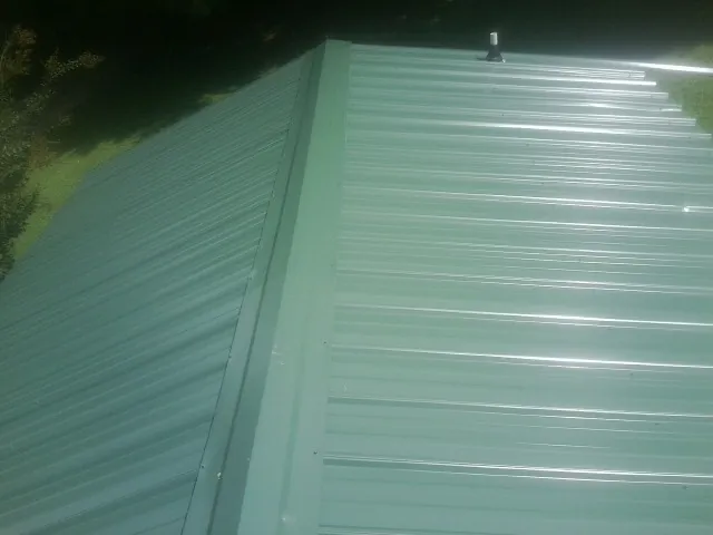 New green metal panels meeting at the ridge of a roof — Flat Roof Repair work by our crew in Bahama