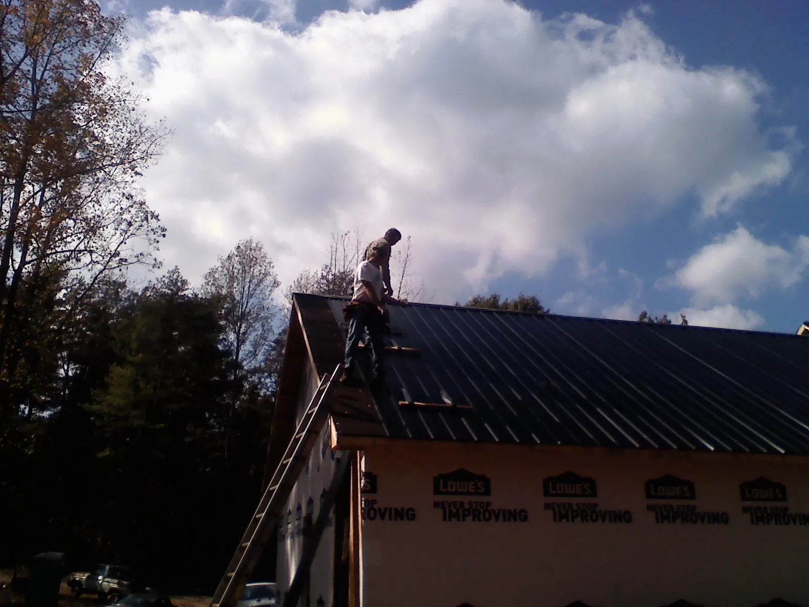 Roofer fastening dark metal panels high against a cloudy sky, from a Roof Inspection job in Bahama