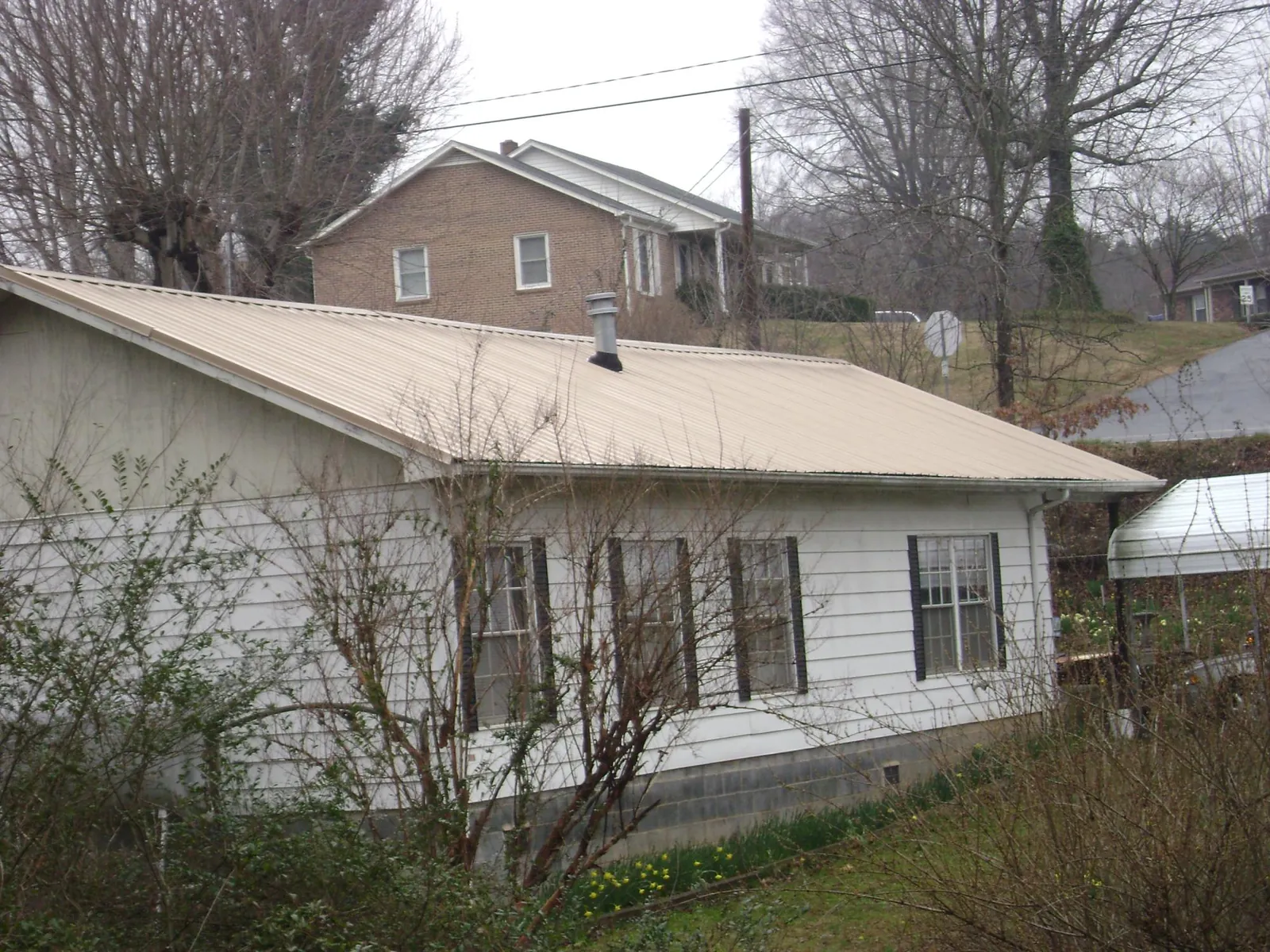 Tan metal roof on a white sided house set into a hillside — Commercial Roofing by Roofing Brothers in Bahama
