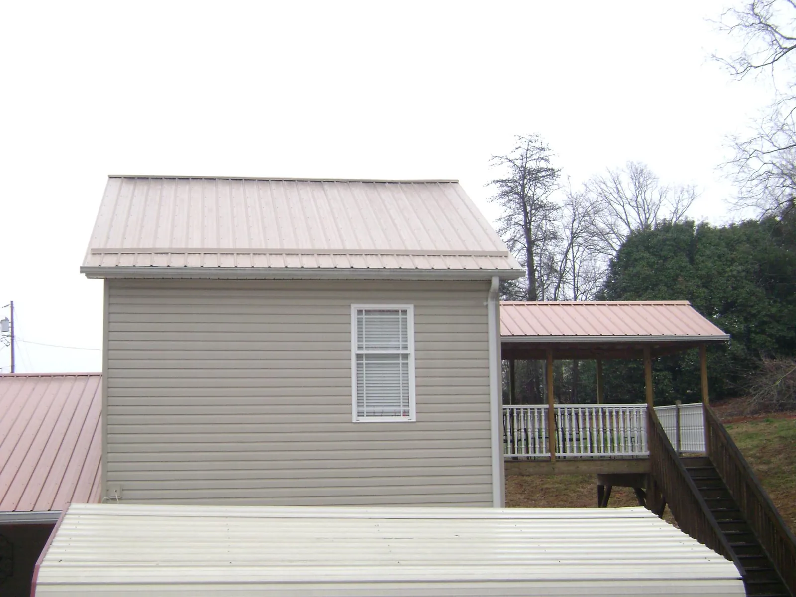 Tan metal roofs on a two story addition and attached porch, from a Roof Replacement job in Bahama